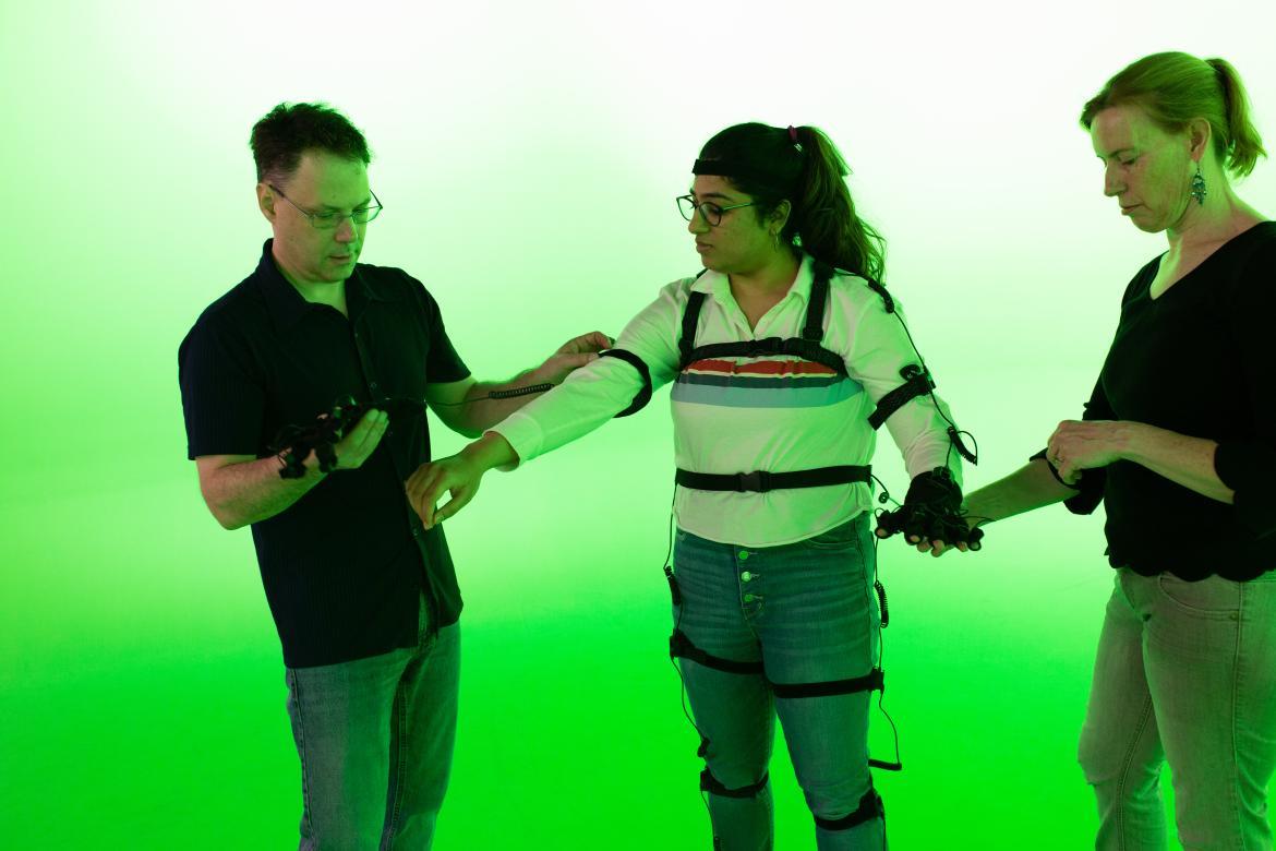student trying out the motion capture suit in the green room with two faculty