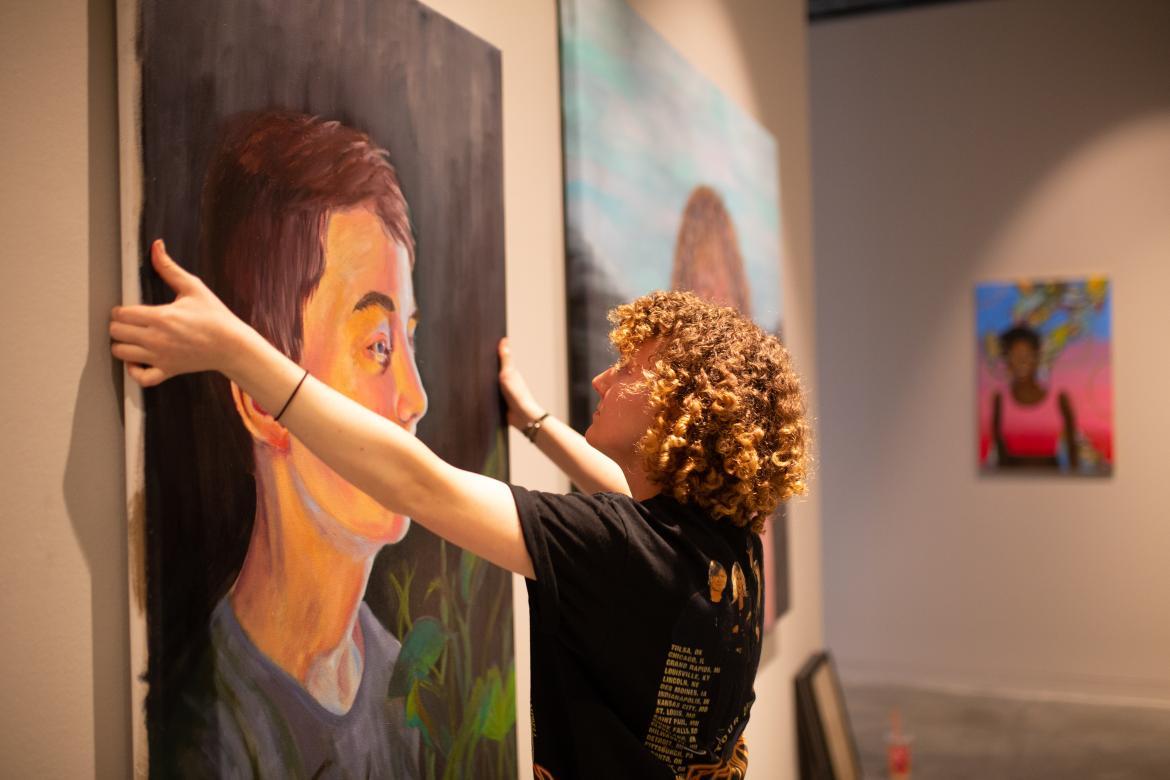 student hanging a large portrait painting on the wall