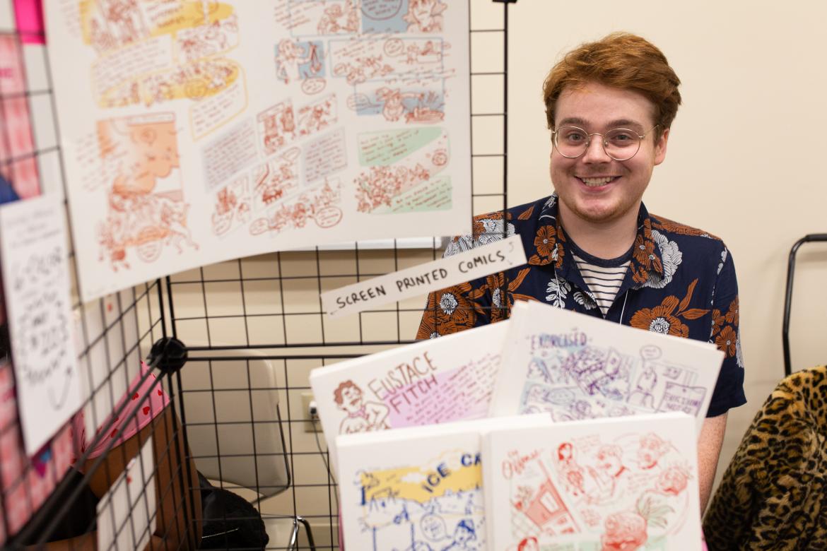 Young man with red hair smiling and selling comic books inside