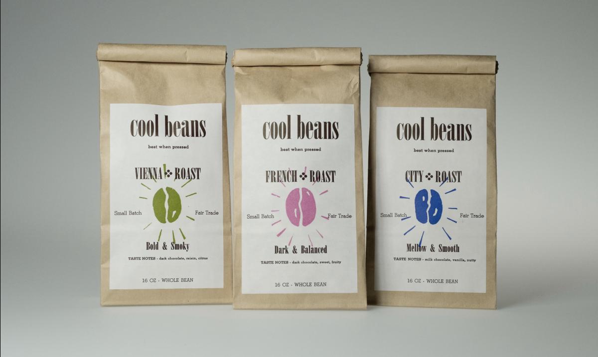 three bags of coffee grounds in brown bags with "Cool Beans" white label on them.