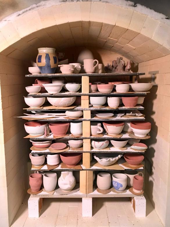 large gas kiln is filled with multiple shelves of ceramic dishes and vessels