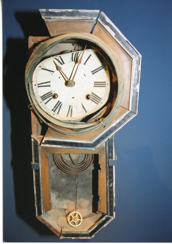 A wall clock that is rusted, cracked and damaged.