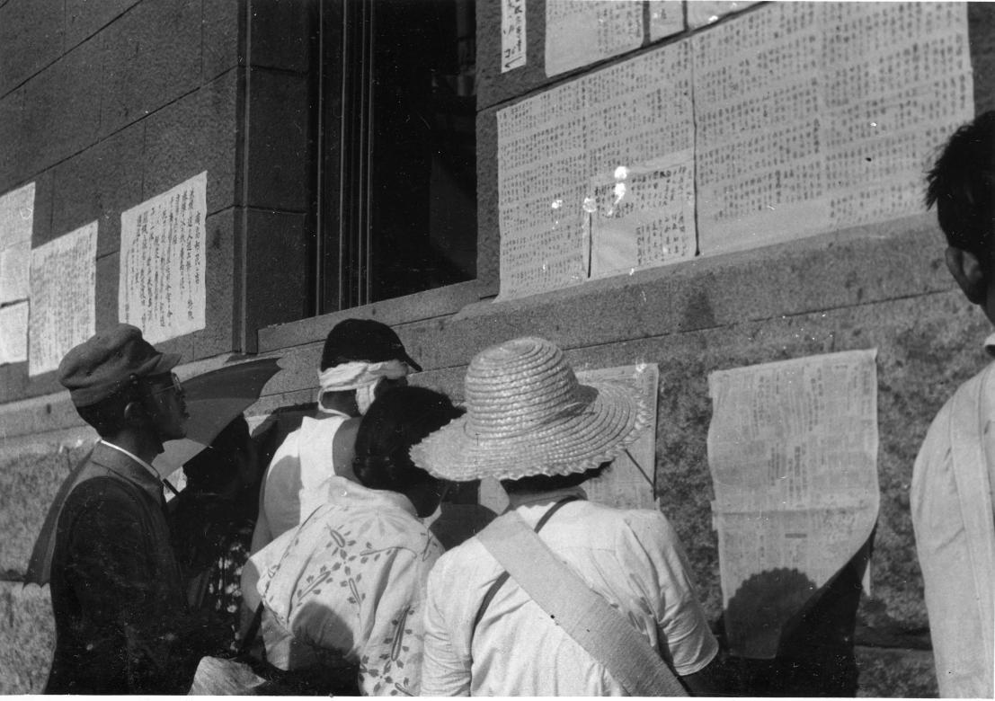 Citizens of Hiroshima and Nagasaki reading postings of a Japanese newspaper on a brick wall outside