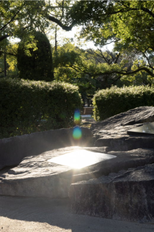 Light seen reflecting through trees shining and reflecting onto a plaque built into a large stone in the Hiroshima Peace Memorial Park.