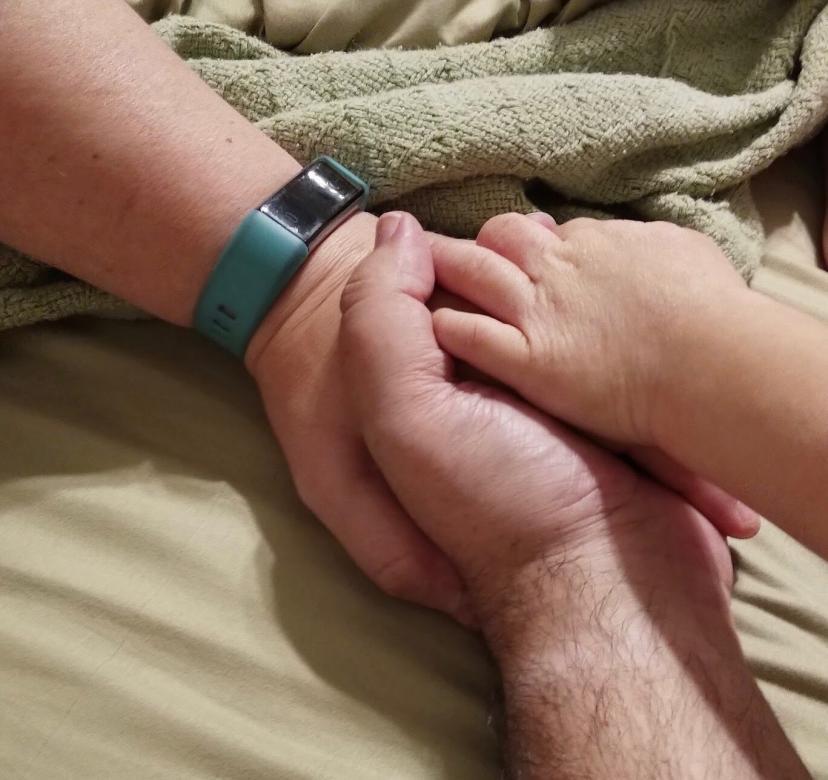 Three hands joined together resting atop a green blanket.