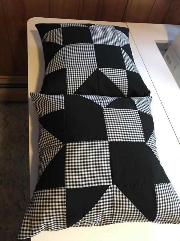 Two sewn pillowcases with 8-point star pattern with black and white/black buffalo plaid fabric laying on a white table. Dimensions 16 inches by 16 inches.