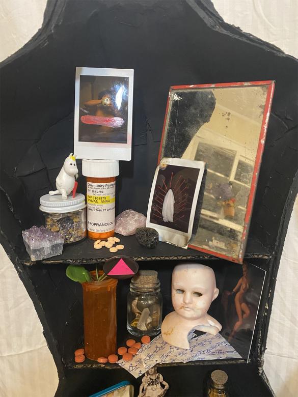 close-up of right half of mannequin, top half, containing trinkets such as a crystal, a mirror, and a pill bottle