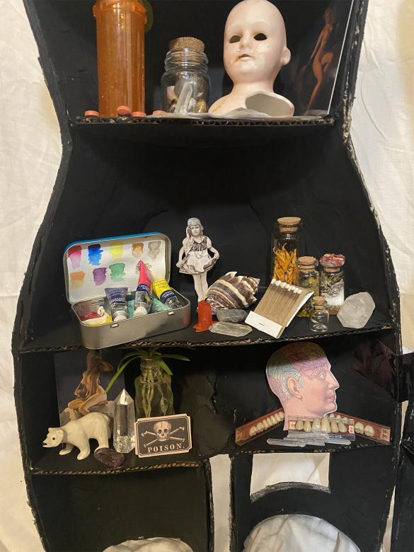 close-up of right half of mannequin, bottom half, containing trinkets such as matches, a plant and teeth