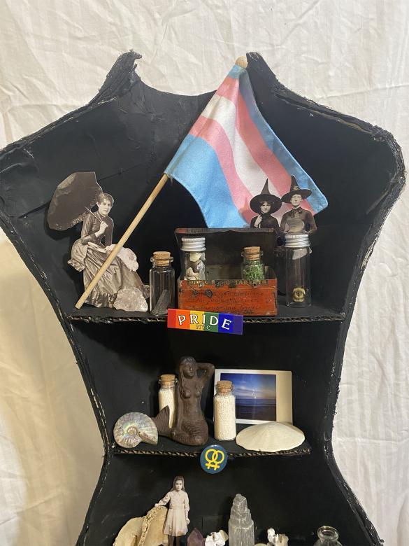 close-up of left half of mannequin, top half, containing trinkets such as a flag, seashells, and a mermaid figurine