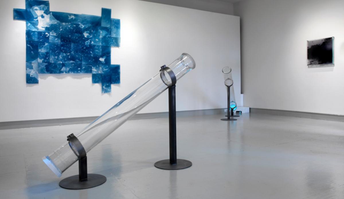 Two clear tubes tilted toward the ceiling in a gallery space. 