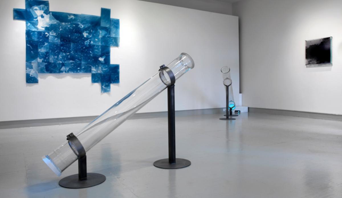 Two clear tubes tilted toward the ceiling in a gallery space. 