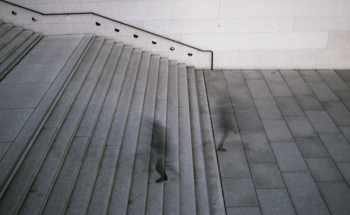 Shot from above of two blurry figures, one going up and the other going down a large cement staircase.