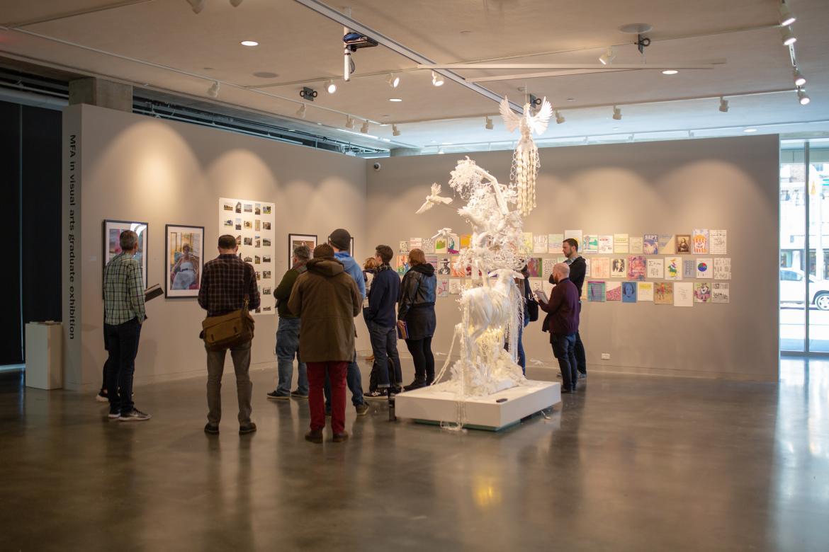 A group of people with notebooks viewing art work in an art gallery. 