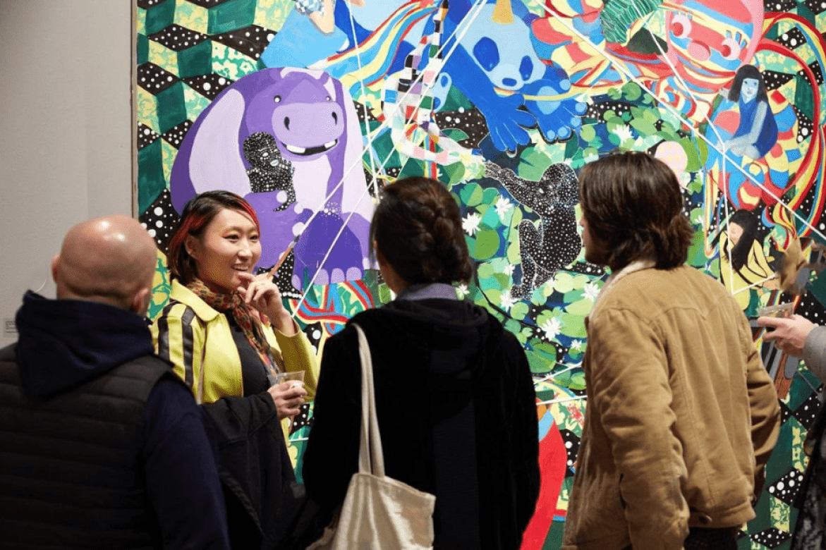 Alumni JooYoung Choi standing in front of her work, talking with visitors at her opening.