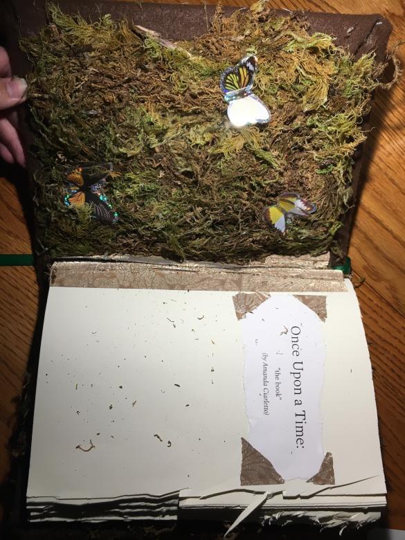 open book on a wood table. One side is the inside cover. The other is a title page, which reads "Once Upon a Time: the book; by Amanda Ciarletto"