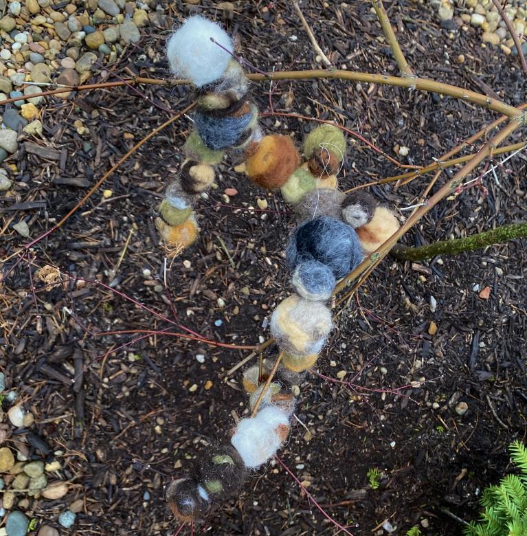 Sculpture comprised of neutral colored wool felted balls. Photographed from above outside in the dirt with branches. 
