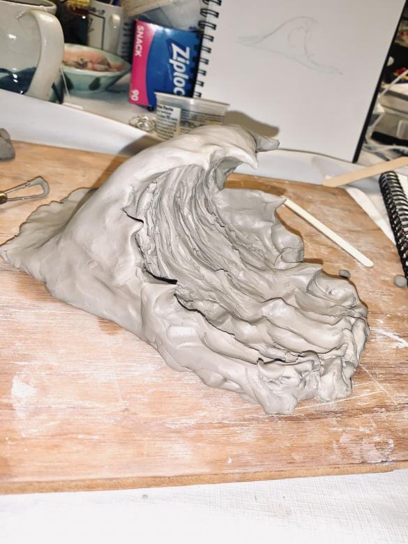 Newly-sculpted model of a large ocean wave beginning to crash, shown in wet clay