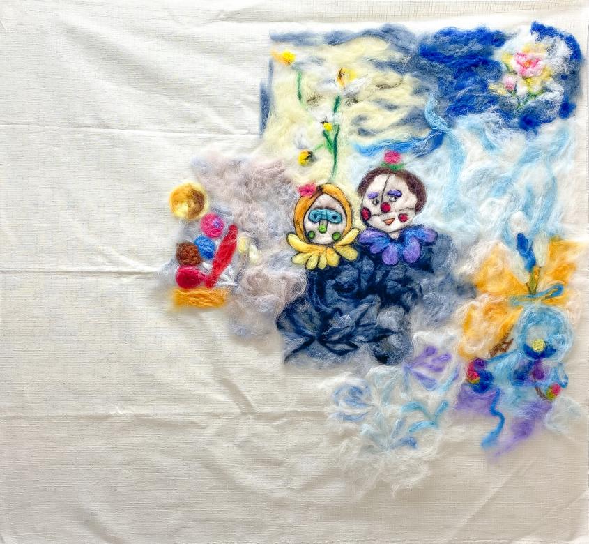 A square of white cloth with a felted image of bright colors in the top right corner. There are blue, white, and light blue swirls throughout with multicolored flowers. In the center of the felt are two clown figures from the bust up with colored colors and face makeup, one has short brown hair while one has shoulder length blonde hair. 