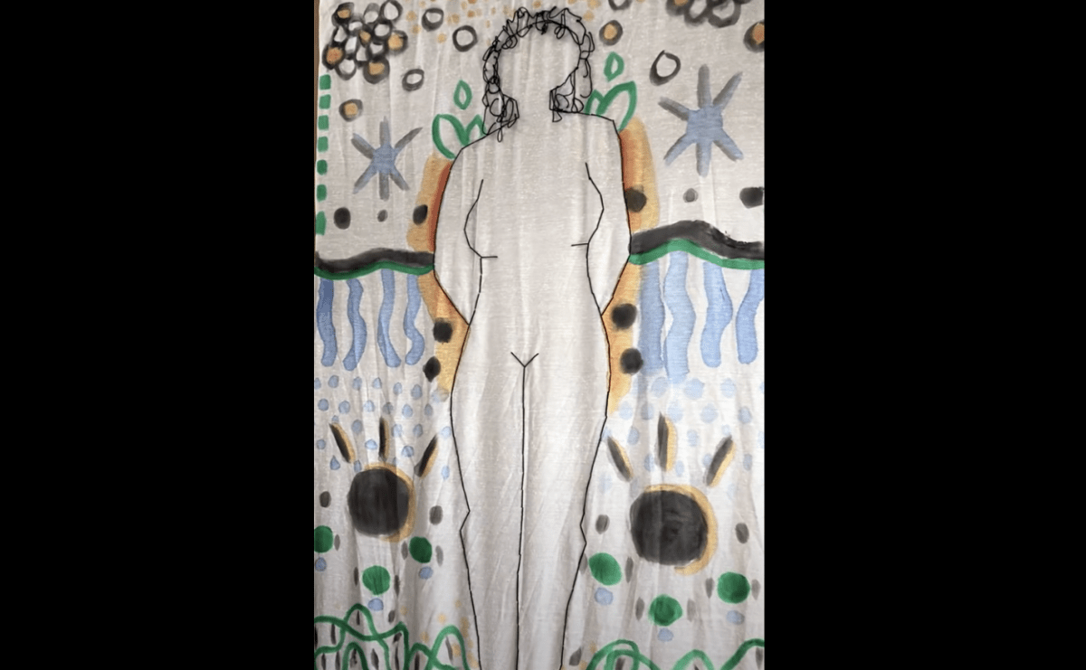 Video still of a large stitched black outline of a figure with no features other than black stringy short hair. Around the figure are orange, blue, green, and black symbols and shapes creating a landscape. 