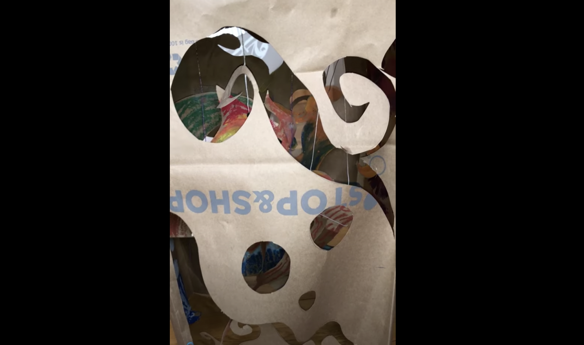 Video still of a brown paper bag with swirls cut out to reveal colorful drawings and yarn inside the bag.
