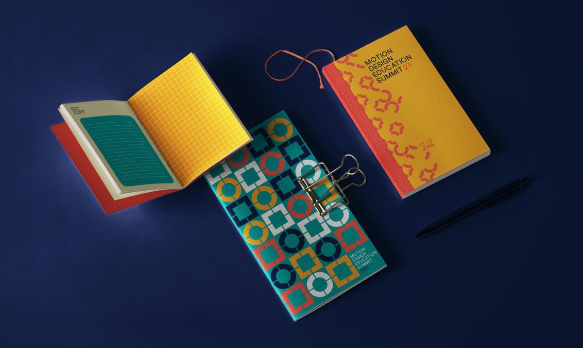 Three small journals that are orange, yellow, teal, dark purple, and white. One journal is open, the other two have covers that are designed with geometric patterns.