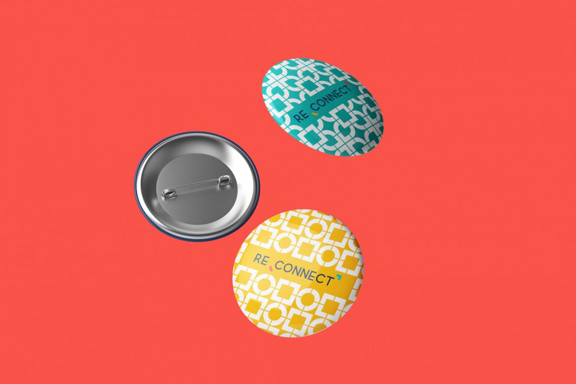 Three pins floating before a peach orange background. The front of two can be seen. Both have a geometric pattern and say "RECONNECT." One is teal the other is yellow.