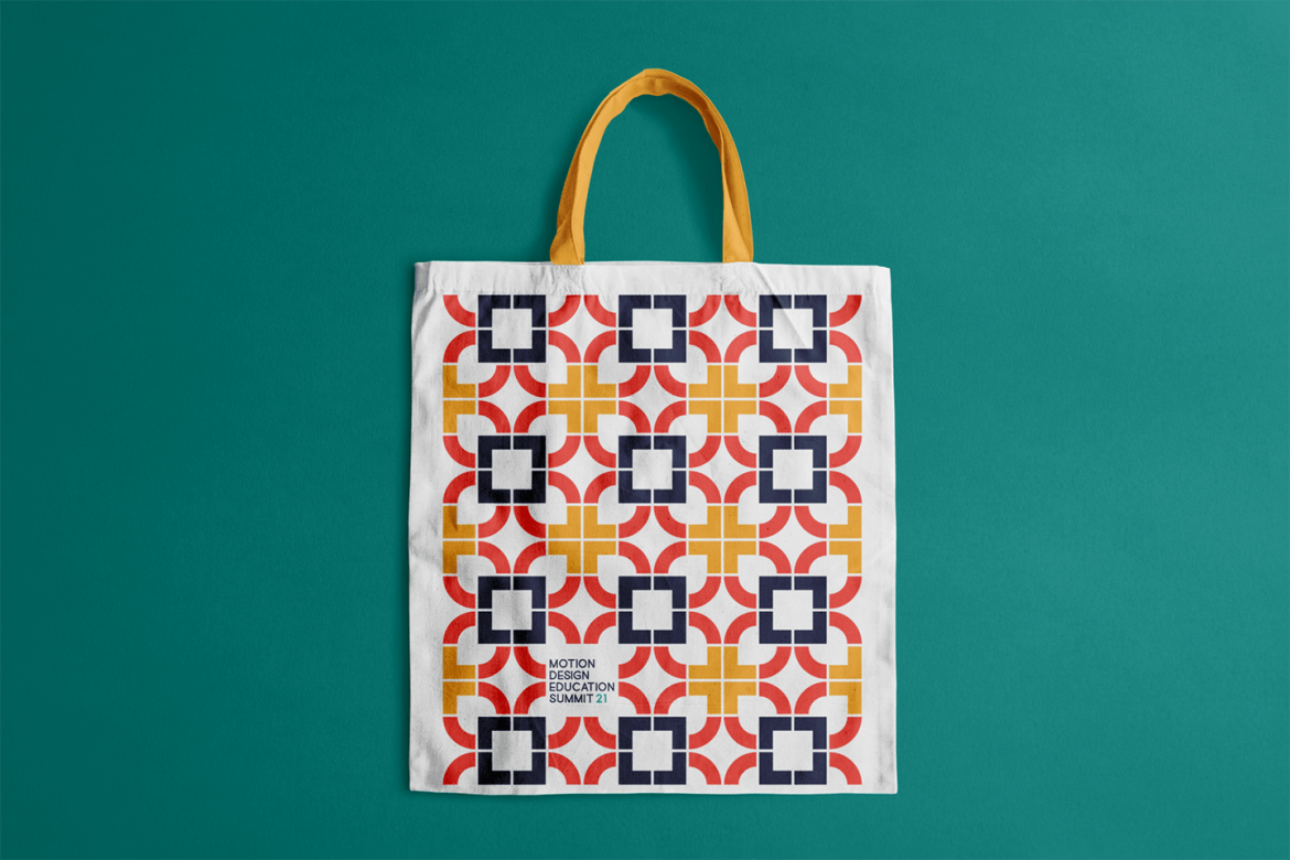 A white tote bag with a yellow, orange, and dark purple geometric pattern. In small type on the tote bag says "Motion Design Education Summit."
