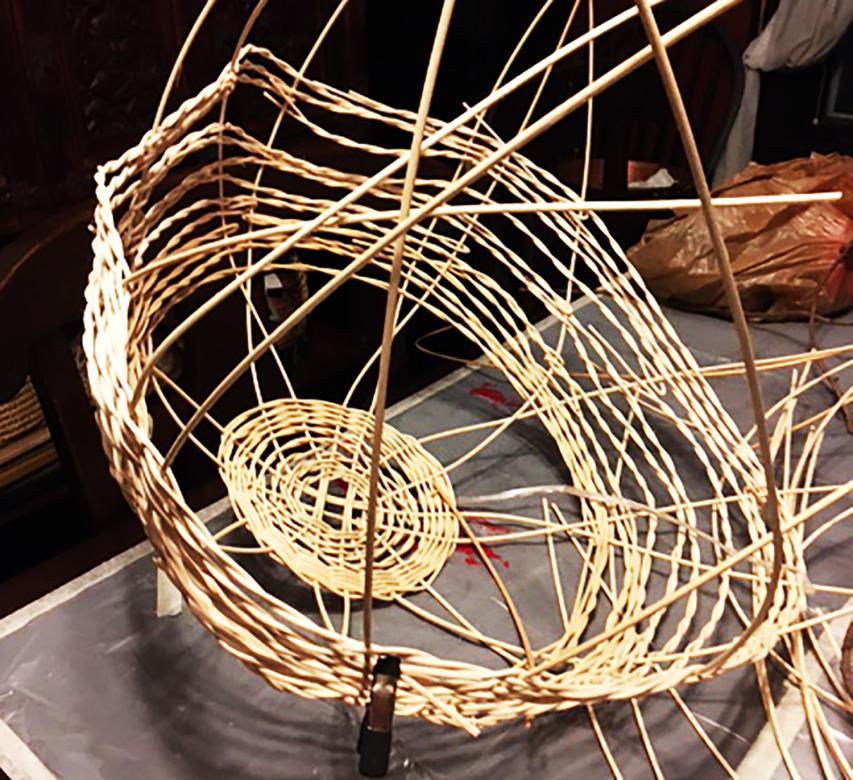Progress photograph of the artist's Nest sculpture forming with reeds woven together to form the start of a sphere. 