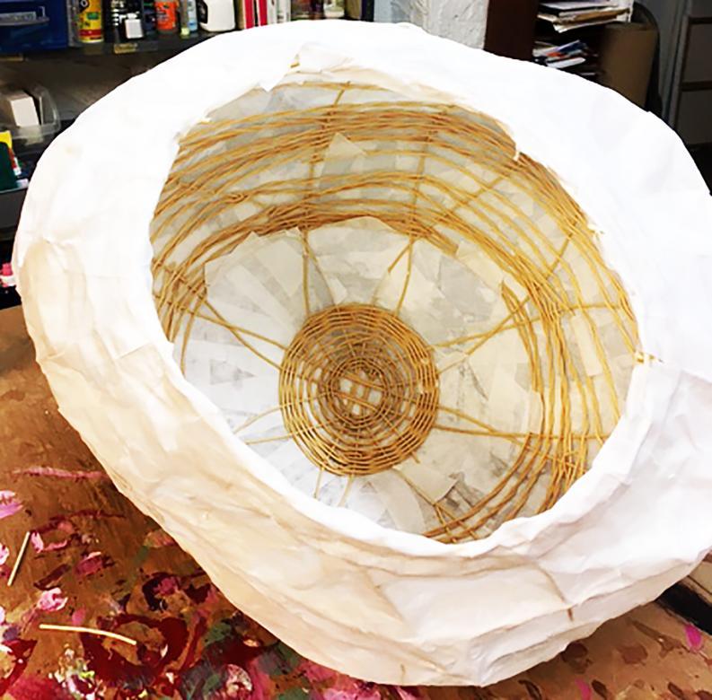 Spherical sculpture made from reed and white rice paper. In this photo, the sculpture is shown incomplete with a view into the sphere of the reeds woven creating the sphere.