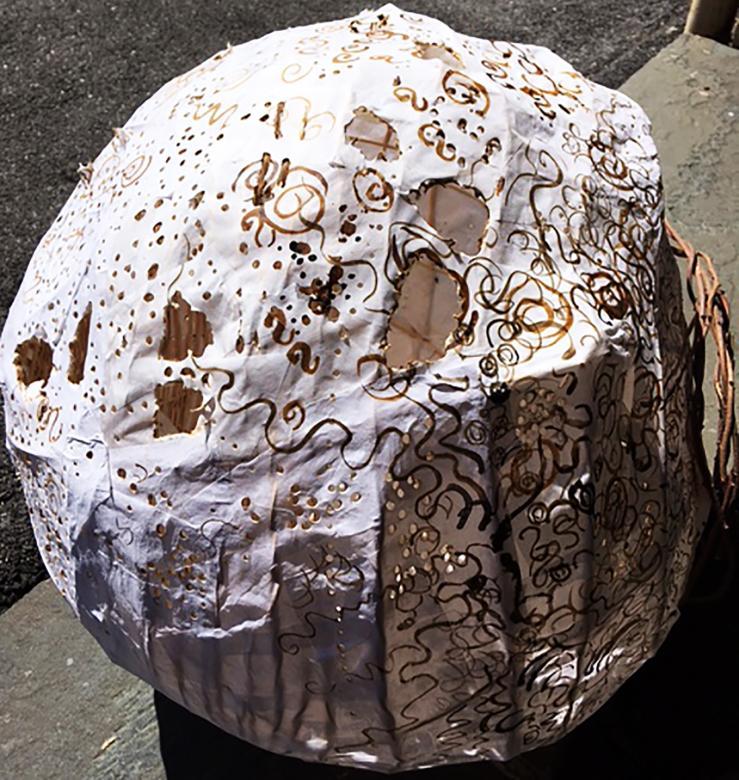 Large spherical sculpture constructed from reed and white rice paper. There are holes exposing the inside of the structure. On the outside, are brown ink drawings of swirls and lines.