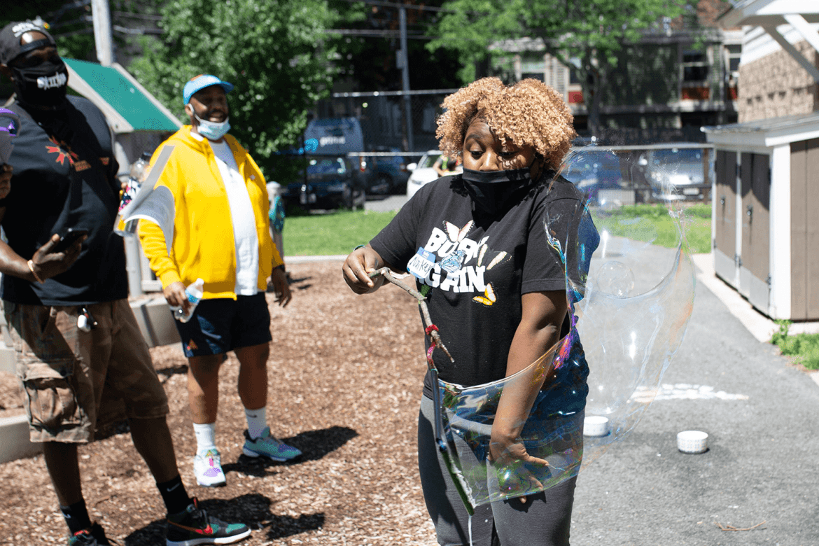 A woman looks surprised while making a huge bubble using a bubble wand made from a stick.