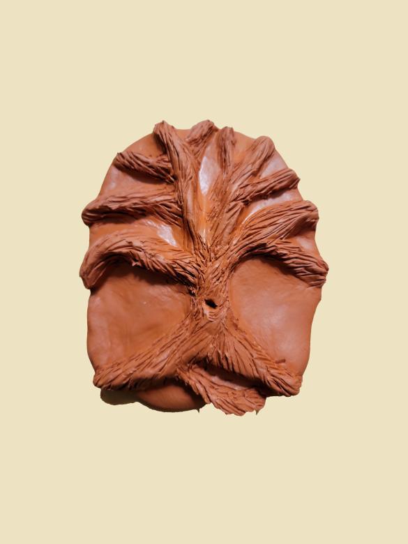 A brown piece of clay with a tree carved out of it. There is a small hole in the trunk of the tree. The tree has no leaves.