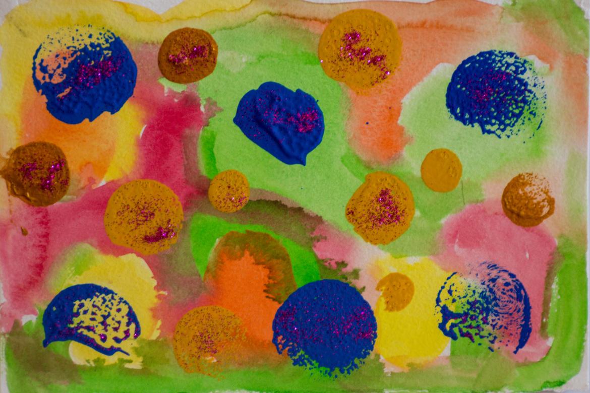 The background is various colors mixed around each other with the colors light green, orange, yellow, and pink. Some of the colors in the background seep into each other. On top of this background are several splotches of blue, mustard yellow, and brown paint. Some of the splotches are dark and distinct and others are lighter. All the splotches have pink glitter on them in varying amounts. 