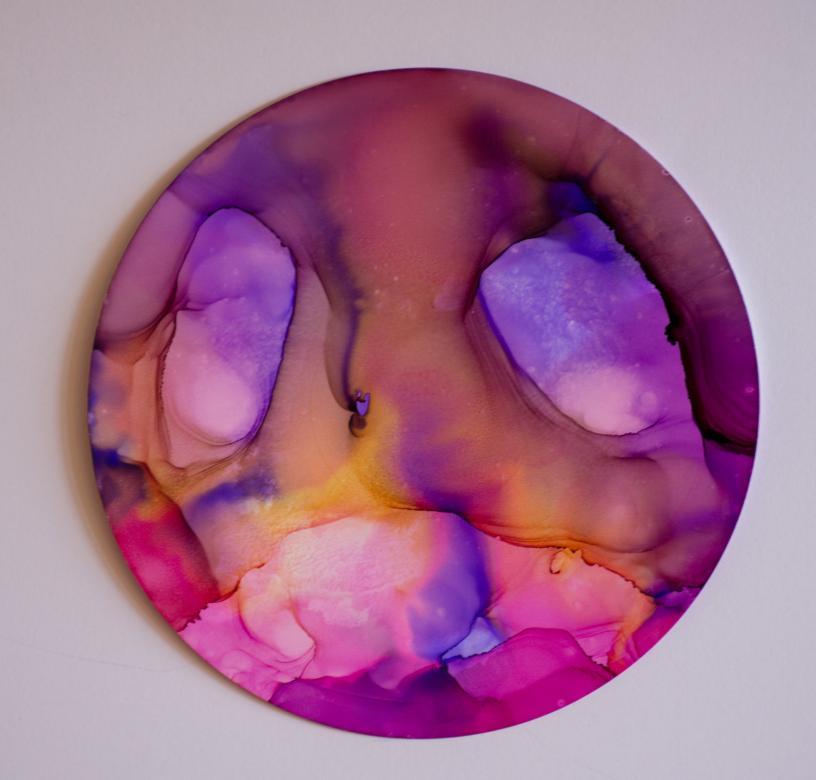 On a circular piece of paper, are the colors orange, blue, pink, and purple. They are all mixed and running together to create some lighter and darker shades of the colors.