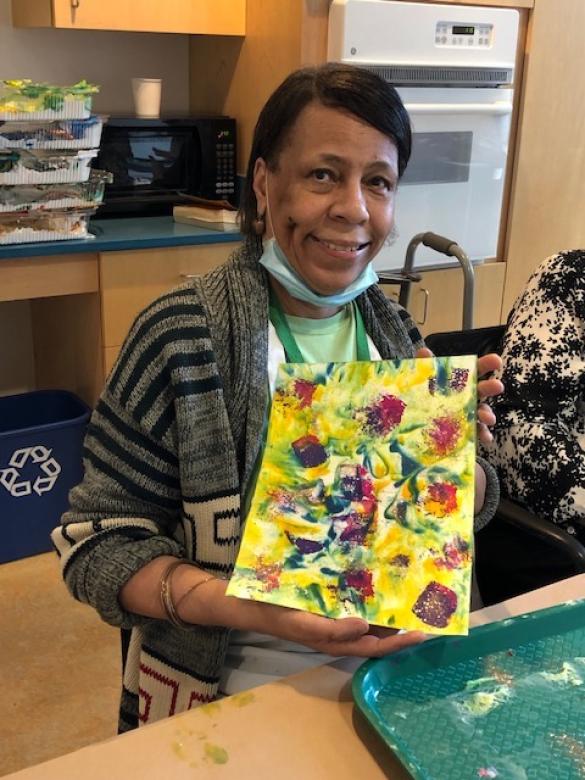 Photograph of artist Cheryl Saunders smiling facing the camera holding a small colorful abstract painting.