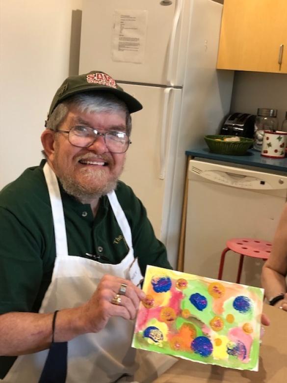 Photograph of artist Davey Fitzgerald smiling facing the camera holding a small colorful abstract painting.