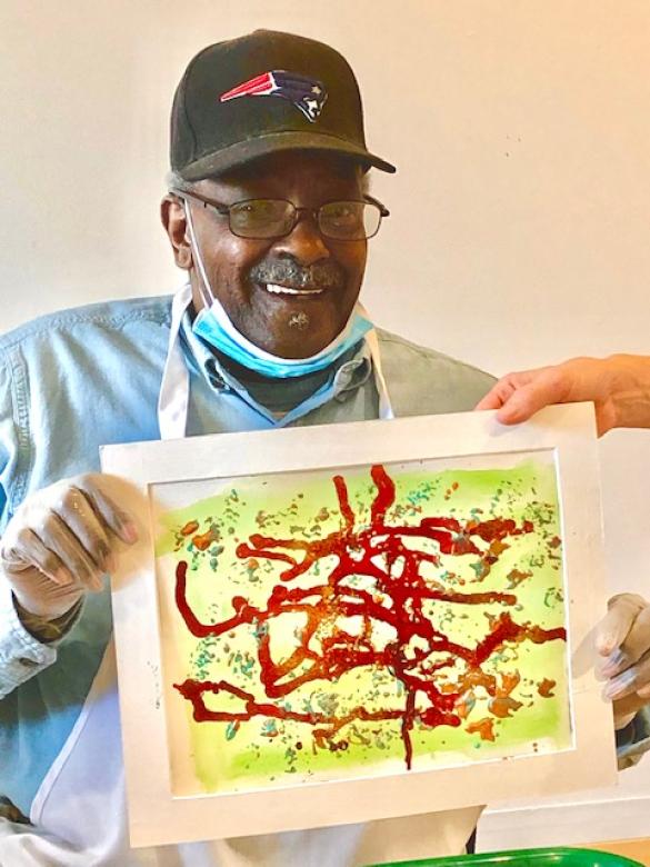 Photograph of artist Douglas Johnson smiling facing the camera holding a small green, yellow, and red abstract painting.