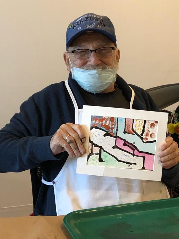 Photograph of artist John Kelly smiling facing the camera holding a small colorful abstract painting.