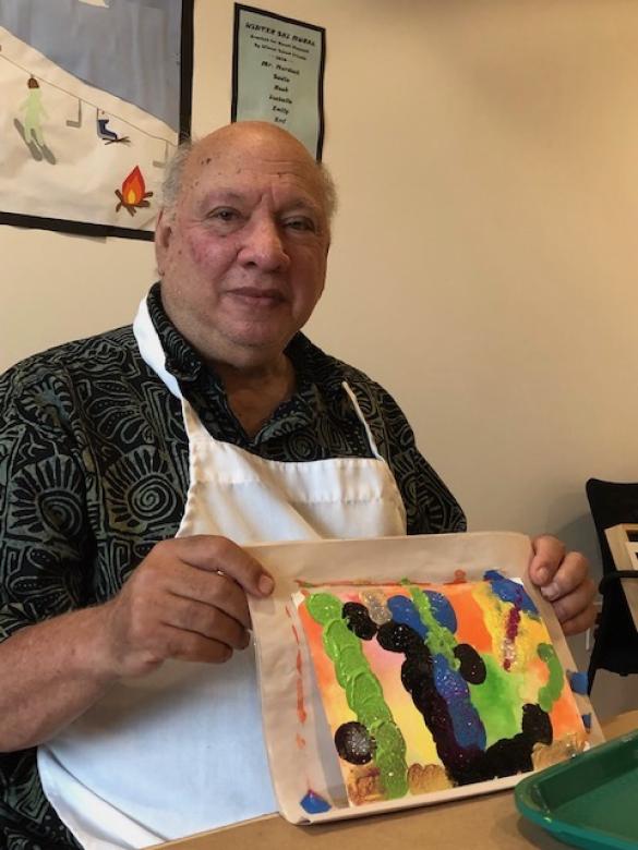Photograph of artist Lanny Johnson smiling facing the camera holding a small colorful abstract painting.