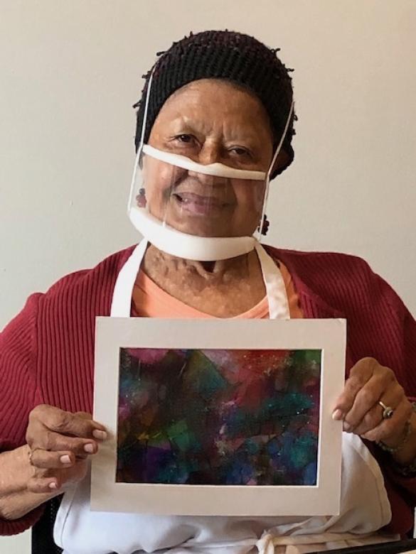 Photograph of artist Lydia Quintera smiling facing the camera holding a small colorful abstract tissue paper collage.