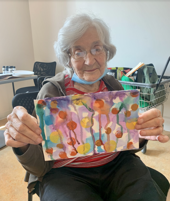 Photograph of artist Judy Esch smiling facing the camera holding a small colorful abstract painting.