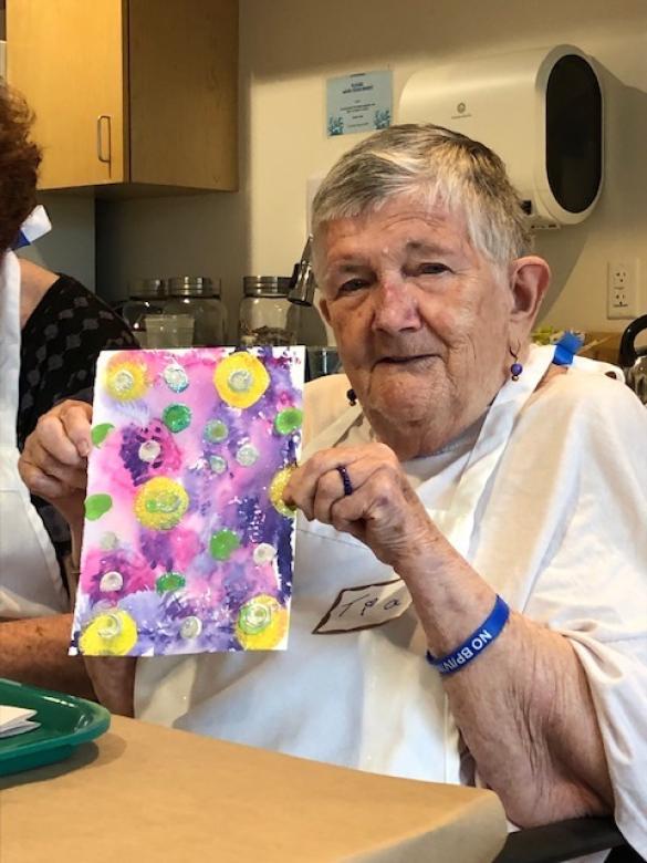 Photograph of artist Tia Hurley smiling facing the camera holding a small colorful abstract painting.