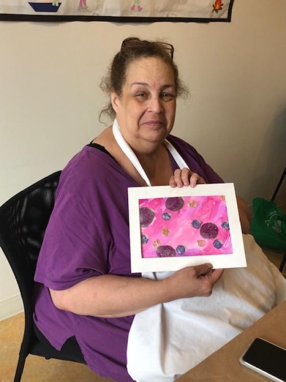Photograph of artist Kim Williams smiling facing the camera holding a small colorful abstract painting.