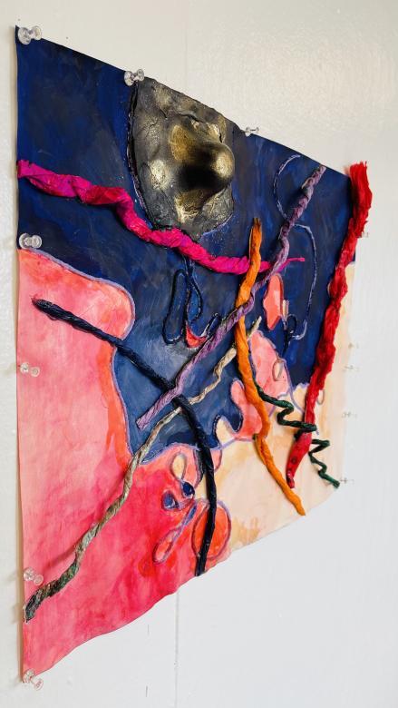 A side view of "Tangled Land" exhibited on the wall, the textured strings and spherical mass can be seen as three dimensional elements on the canvas. 