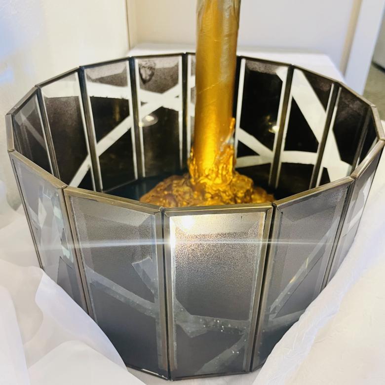 Close up of "The Internals" mixed media sculpture showing the bottom layer of glass rectangular panels painted black with clear translucent stripes revealing the gold mass holding up the golden pole in the center of the sculpture.