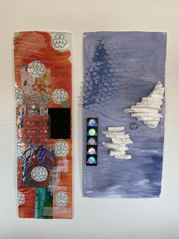 Against a white wall are two rectangles made from recycled and found materials. On the left, is an orange rectangle with pops of blue, black, and green in addition to green recycling signs shining through. On the right is a pale blue rectangle adorned with styrofoam, chicken wire, and silver metallic material.