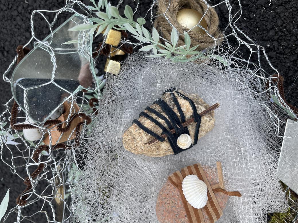 Close up of the white tulle, and chicken wire housing rocks and shells wrapped together within the sculpture "Self-Portrait". Mirrored objects reflect the shells and greenery wrapped into the chicken wire. 