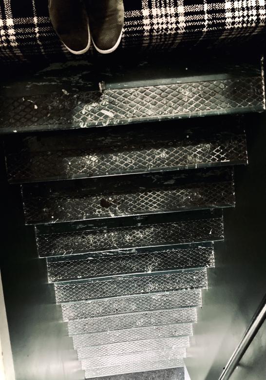 Photo of someone's shoes at the top stair, looking down a black staircase
