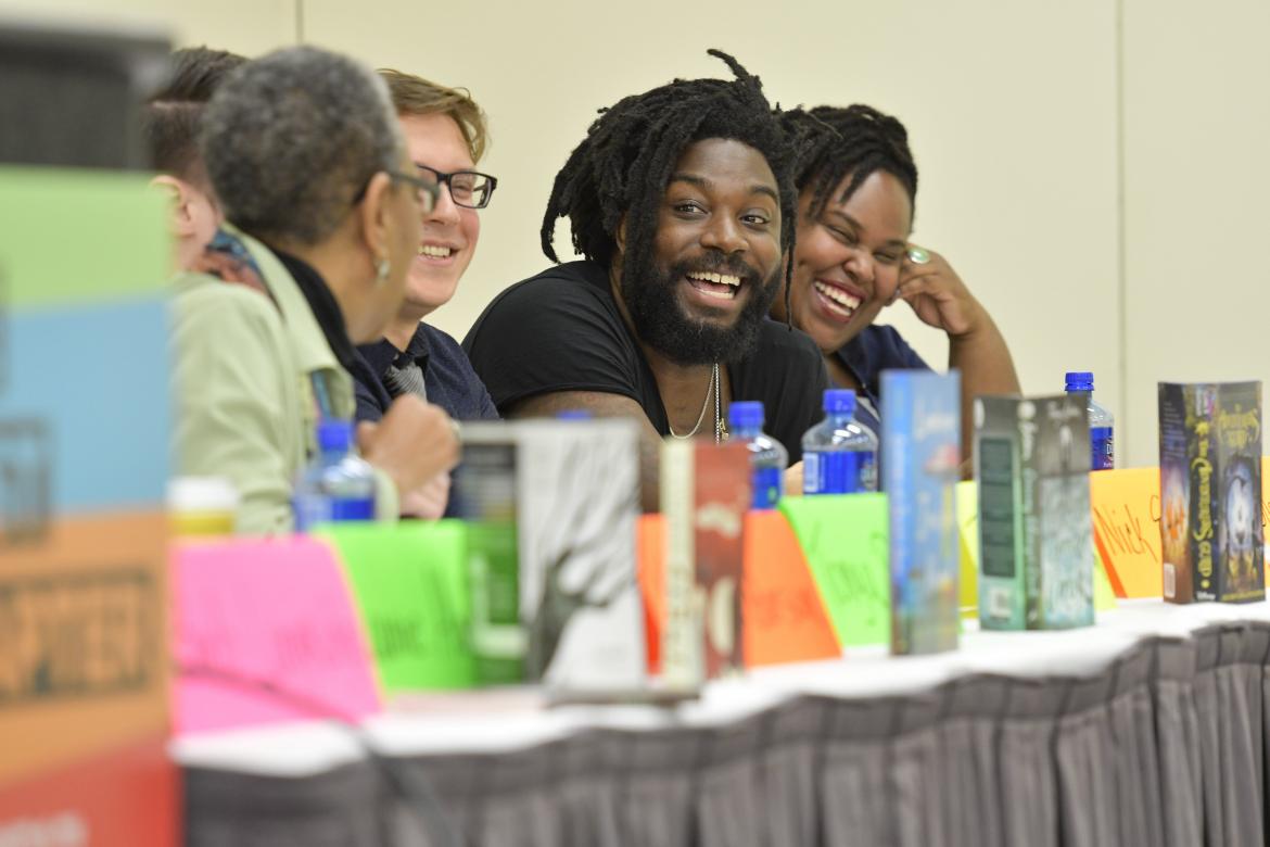 Jason Reynolds smiles as he sits on a panel with fellow authors.