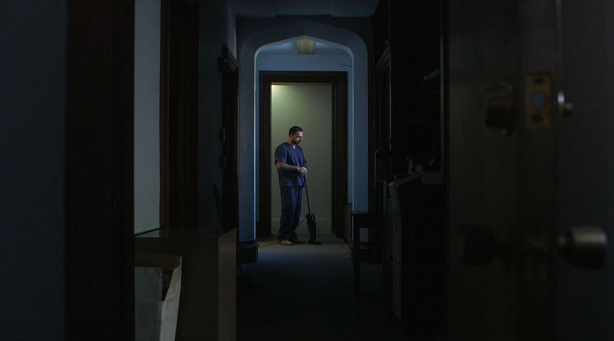 A person stands in a doorway in the distance of dark house